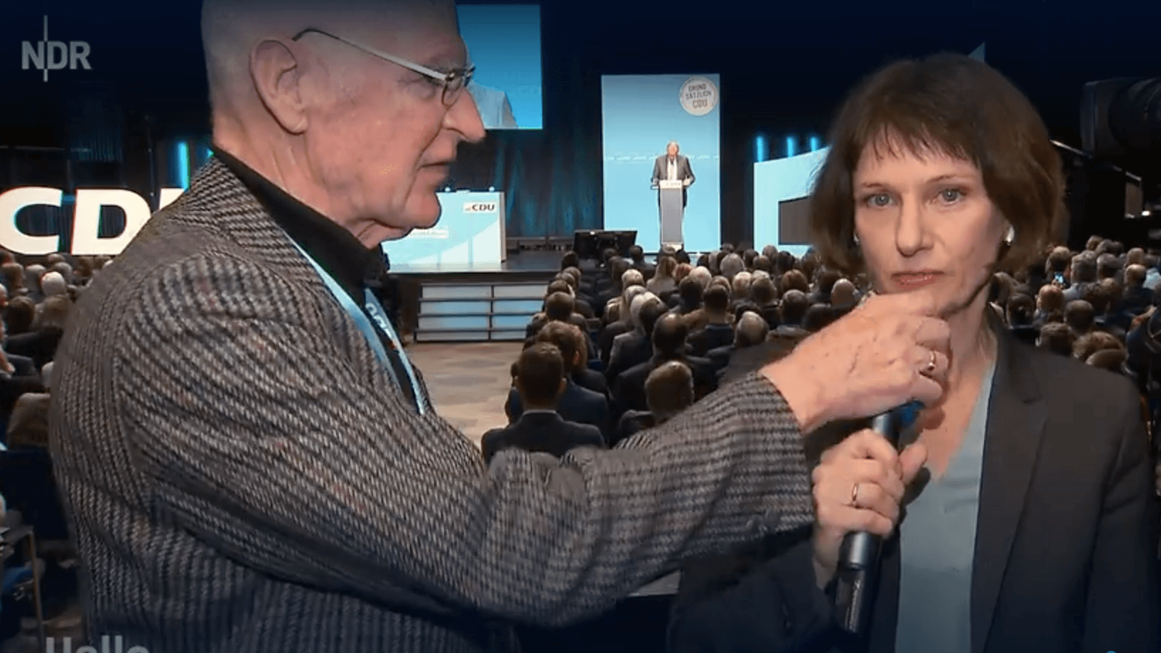 Ein Mann greift NDR-Reporterin Katharina Seiler bei einer CDU-Regionalkonferenz ins Mikrofon.