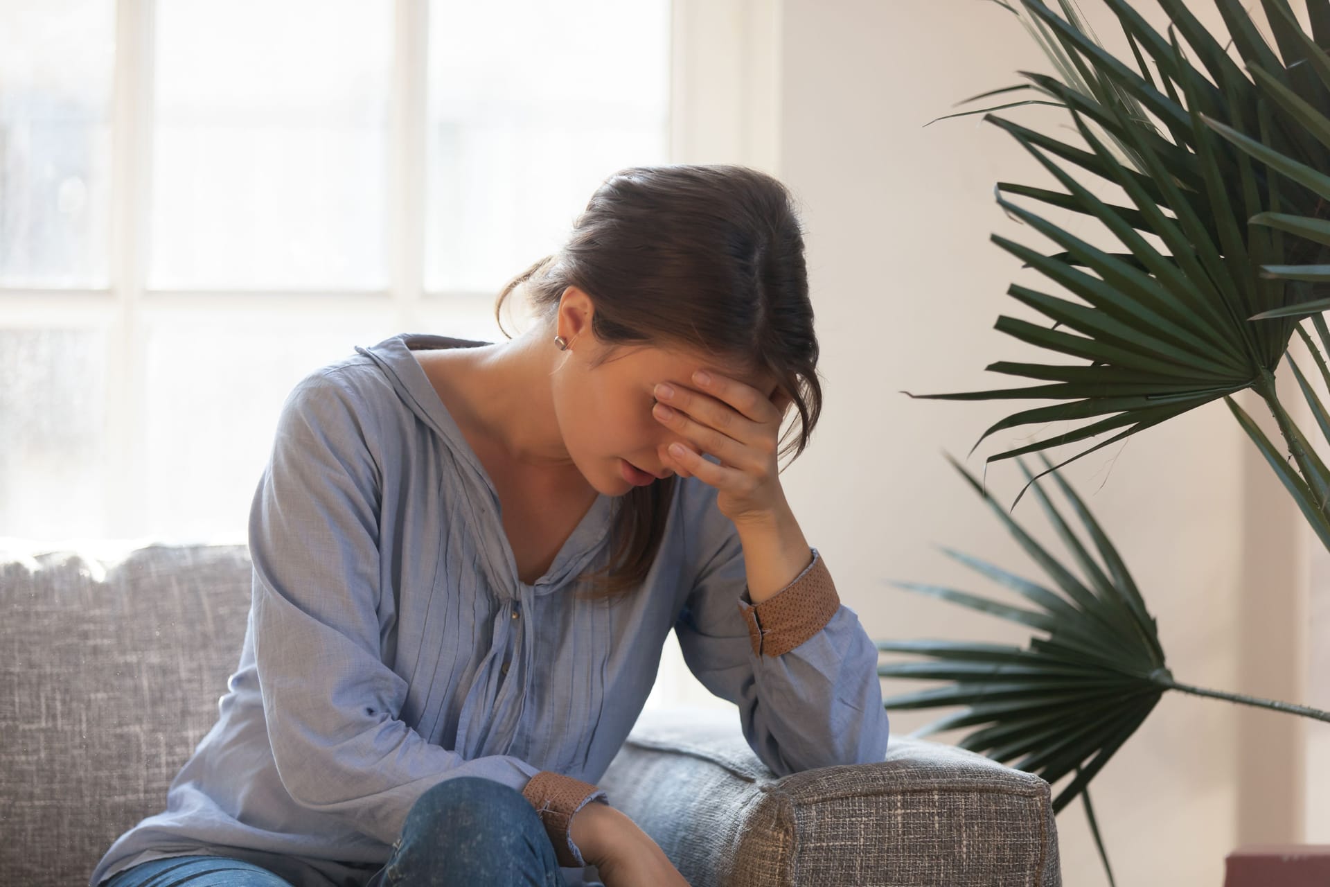 Eine Frau sitzt auf dem Sofa und stützt den Kopf auf die Hand.