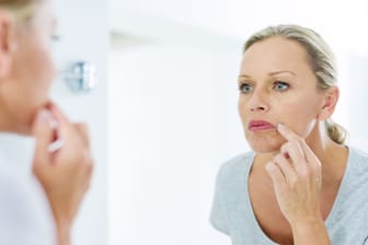 Frau inspiziert ihre Gesichtshaut vor dem Badezimmerspiegel.