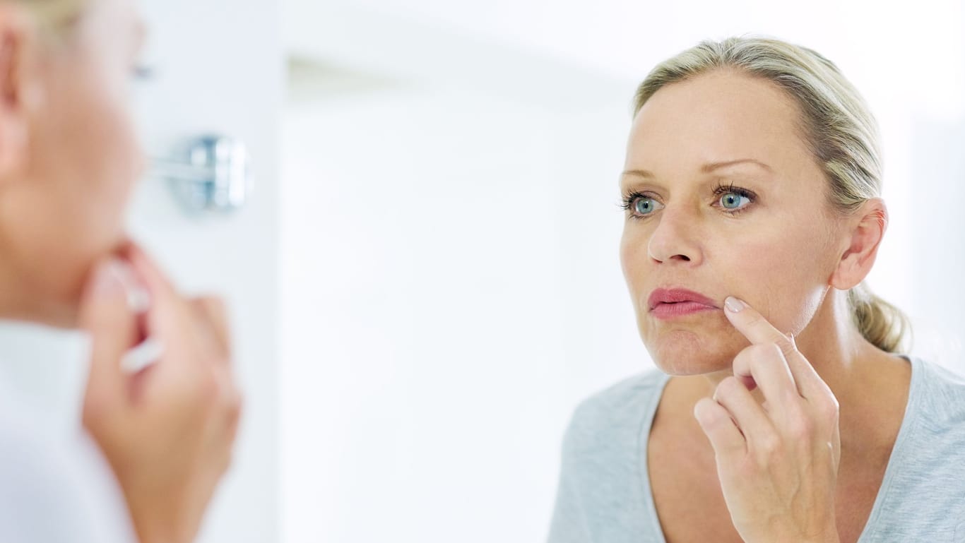Frau inspiziert ihre Gesichtshaut vor dem Badezimmerspiegel.