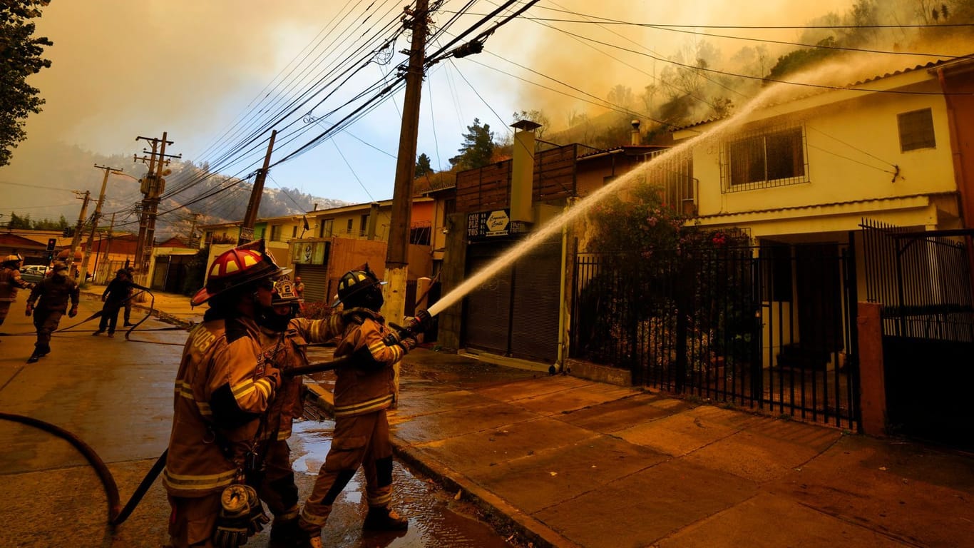 Feuerwehrleute spritzen Wasser auf ein Haus in Chile: Waldbrände haben Tausende Häuser zerstört.