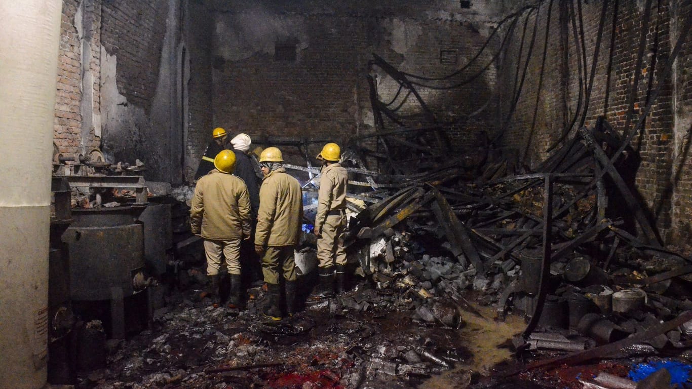 Feuerwehrleute schauen zu, nachdem sie am späten Donnerstag ein Feuer in einer Farbenfabrik im Stadtteil Alipur im Norden von Neu-Delhi, Indien, gelöscht haben.