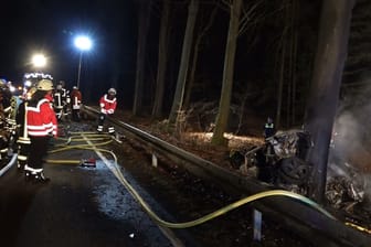 Einsatzkräfte der Feuerwehr löschen das brennende Auto des Toten. Der Mann war zuvor gegen einen Baum geprallt und in seinem Wagen verbrannt.