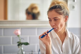Nachdenkliche Frau beim Zähneputzen: Wenn es trotz regelmäßiger Zahnhygiene immer wieder zu Karies kommt, kann das am Zähneputzen liegen und/oder andere Gründe haben.