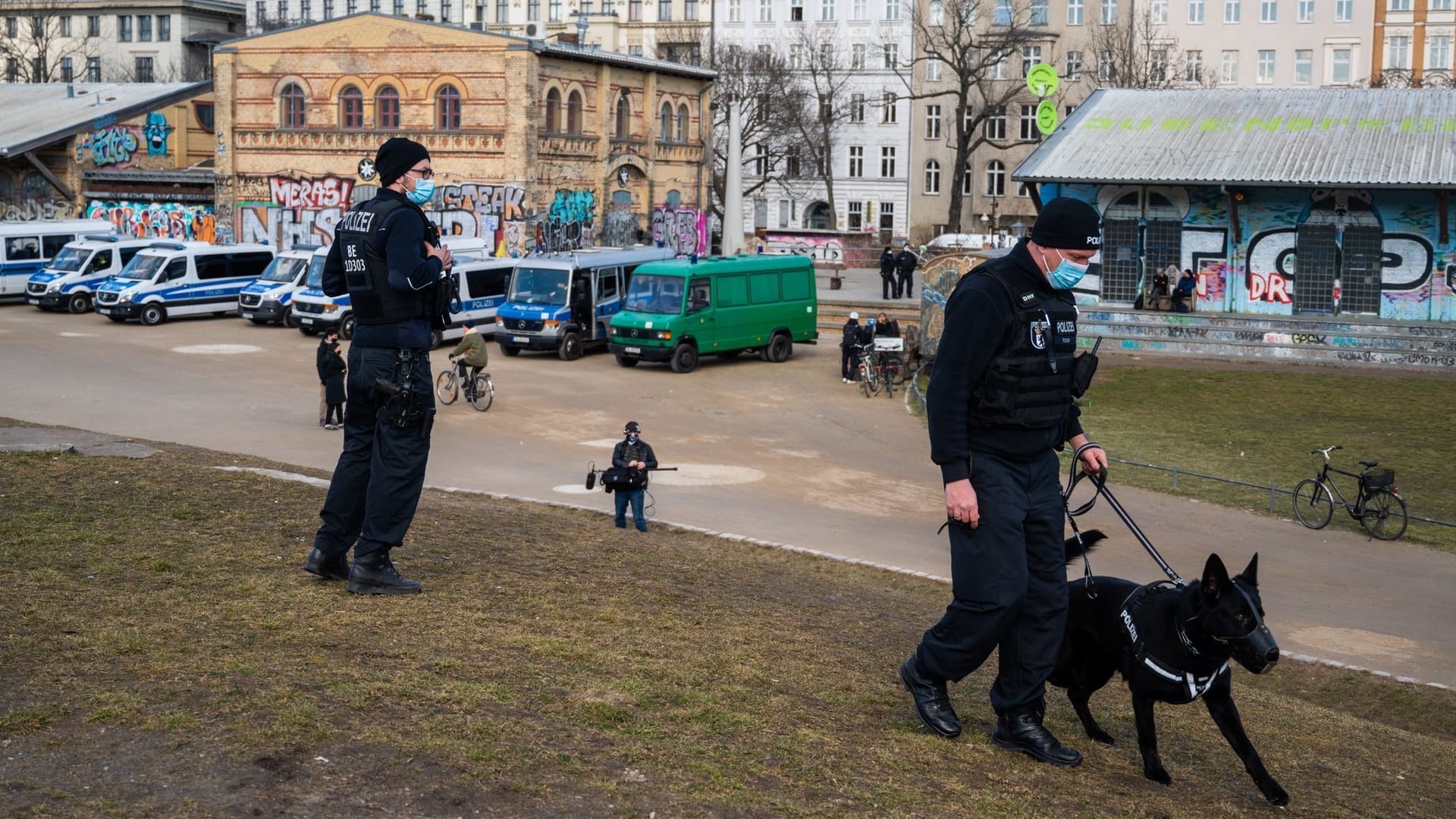 Zwei Polizisten und ein Polizeihund stehen bei einem Polizeieinsatz im Görlitzer Park.