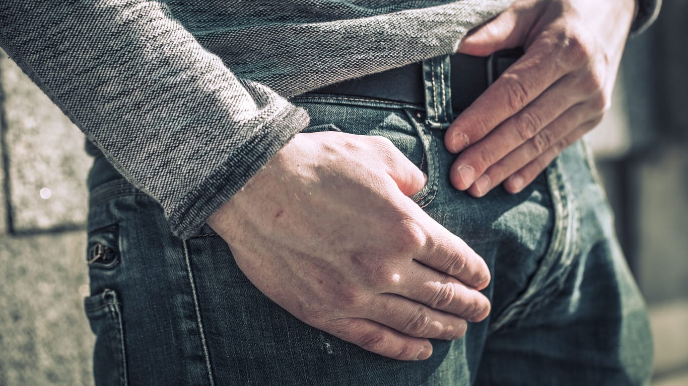 Ein Mann in Jeans hält eine Hand über seiner rechten Leiste