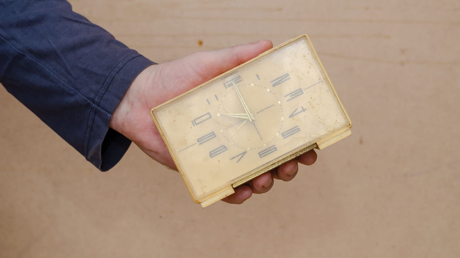 A mature man is holding an old rectangular clock in his hand. Th