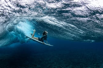 Eine Surferin taucht am Veranstaltungsort der olympischen Surfwettbewerbe auf Tahiti unter einer Welle durch: Für Olympia will Frankreich ein Korallenriff zerstören.