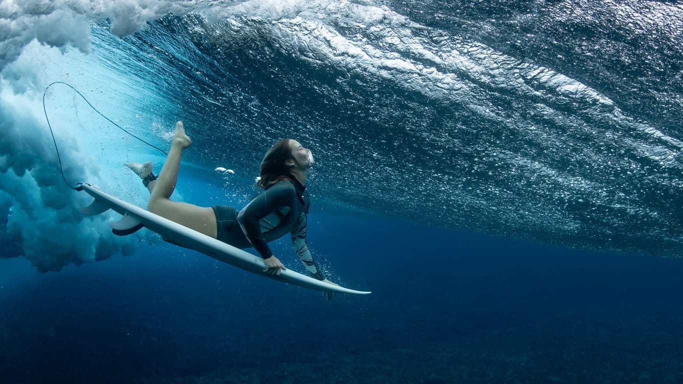 Eine Surferin taucht am Veranstaltungsort der olympischen Surfwettbewerbe auf Tahiti unter einer Welle durch: Für Olympia will Frankreich ein Korallenriff zerstören.