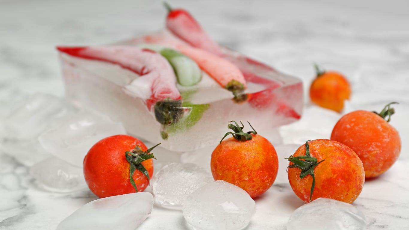 Frozen vegetables and ice cubes on marble table