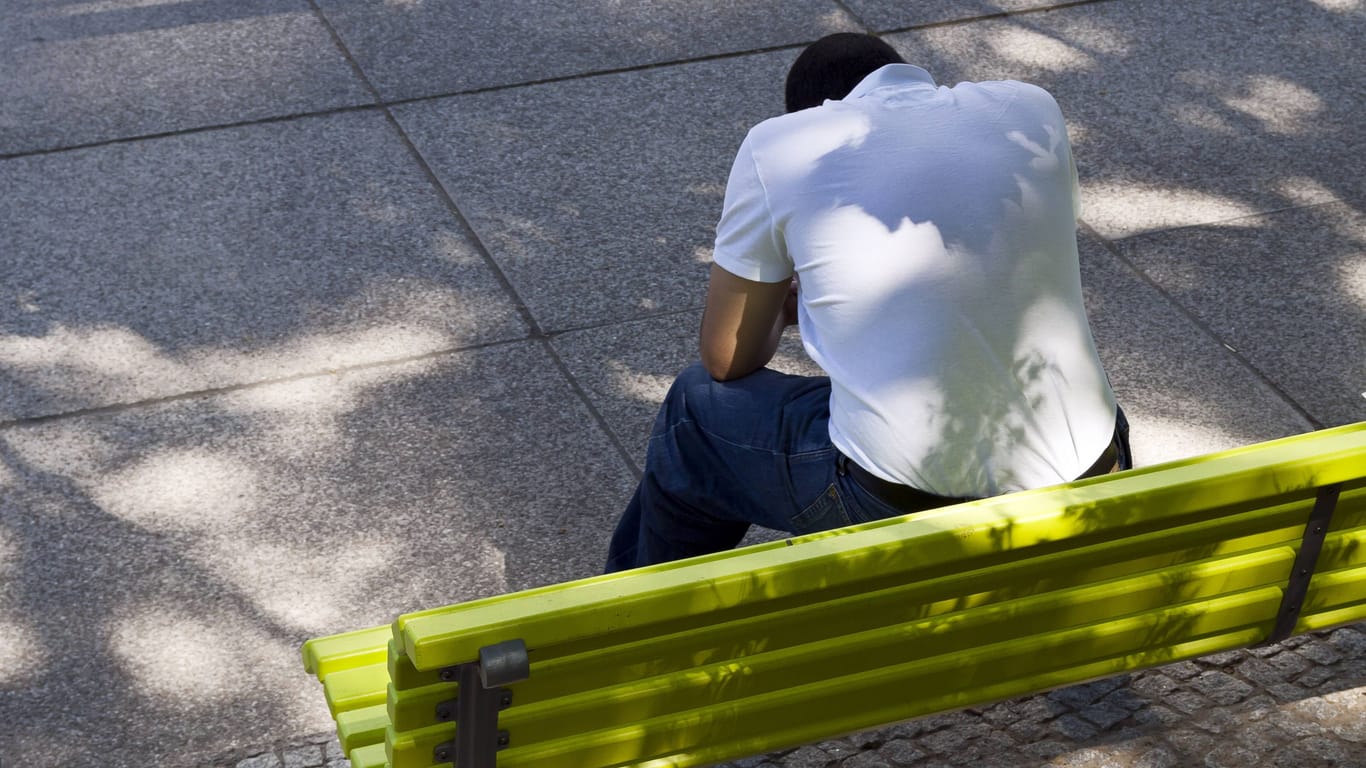 Ein Mann mit gesenktem Haupt sitzt auf einer grünen Parkbank: Bei Depressionen sind zuletzt auch immer mehr junge Männer betroffen.