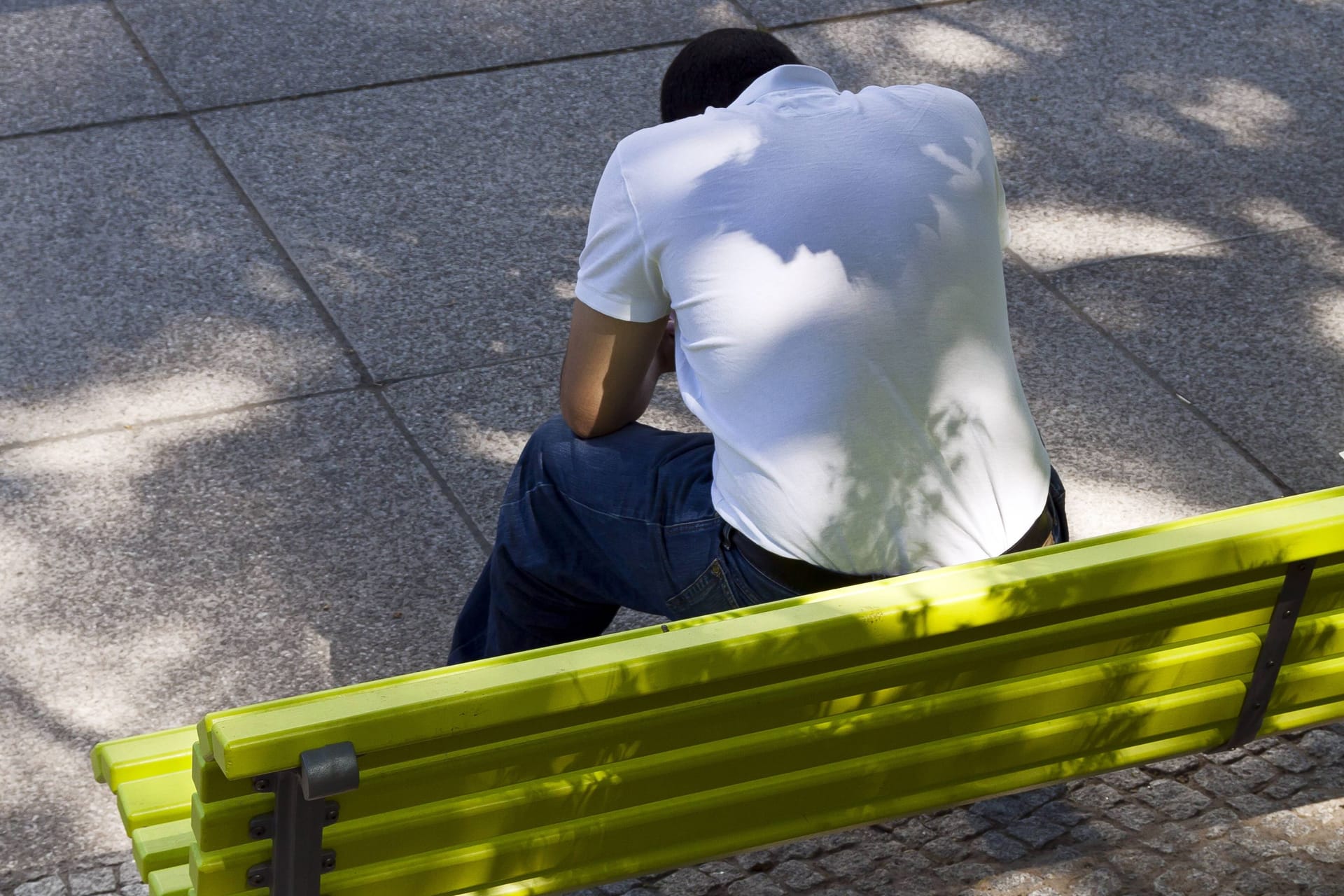 Ein Mann mit gesenktem Haupt sitzt auf einer grünen Parkbank: Bei Depressionen sind zuletzt auch immer mehr junge Männer betroffen.