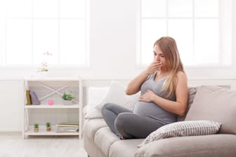 Schwangere Frau sitzt auf dem Sofa und leidet unter Übelkeit