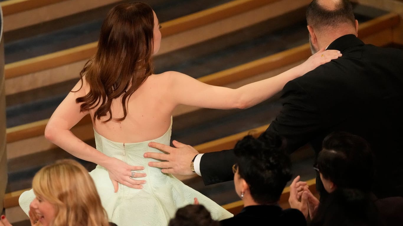 Vorsichtige Schritte auf die Bühne: Emma Stone hält sich mit einer Hand das Kleid am Rücken zusammen.