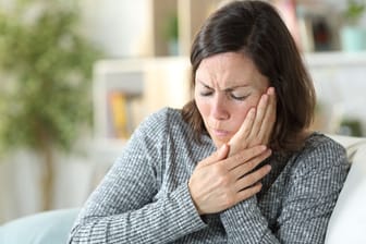 Frau mit Gesichtsschmerzen: Liegt eine bestimmte anatomische Anomalie vor, können bestimmte Kopfbewegungen Schmerzen im Gesicht, im Kiefer- oder Ohrbereich auslösen.