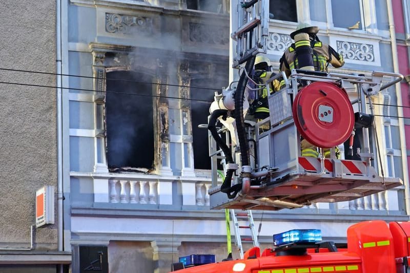 Feuerwehrleute stehen vor dem Solinger Mehrfamilienhaus, in dem es gebrannt hat: Am Montagvormittag wurde noch ein Kleinkind nach dem Brand vermisst.