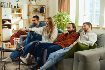 One young woman in friends young male company switches decisive soccer game seated on couch in living room at home. Concept of leisure activity.