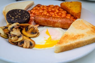 White board with full English breakfast with bacon, fried egg, beans, tomato, roasted sausage, black pudding, scons, hash browns and fried mushrooms