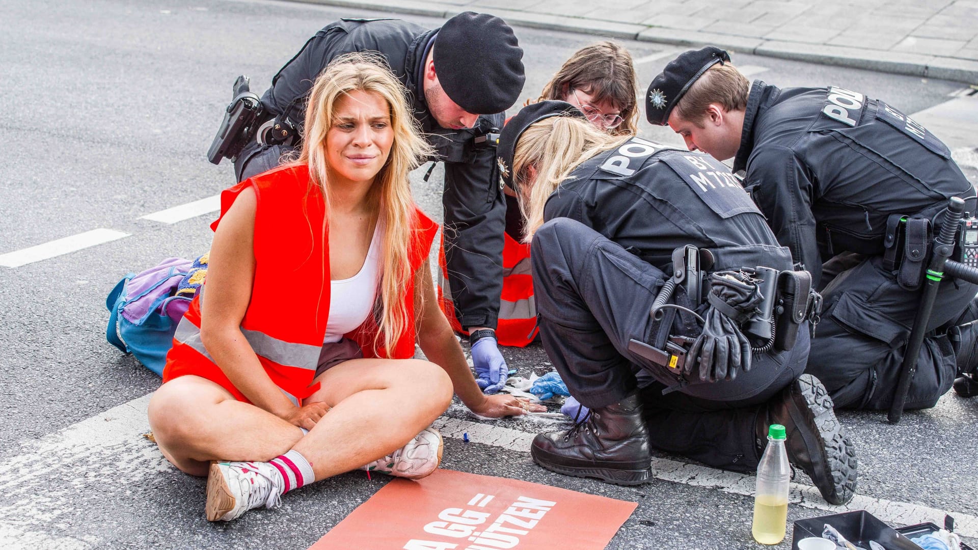 Ein Polizist versucht die Hand von Anja Windl von der Straße zu lösen: Die Klimaaktivisten will vor Gericht auf einen Anwalt verzichten.