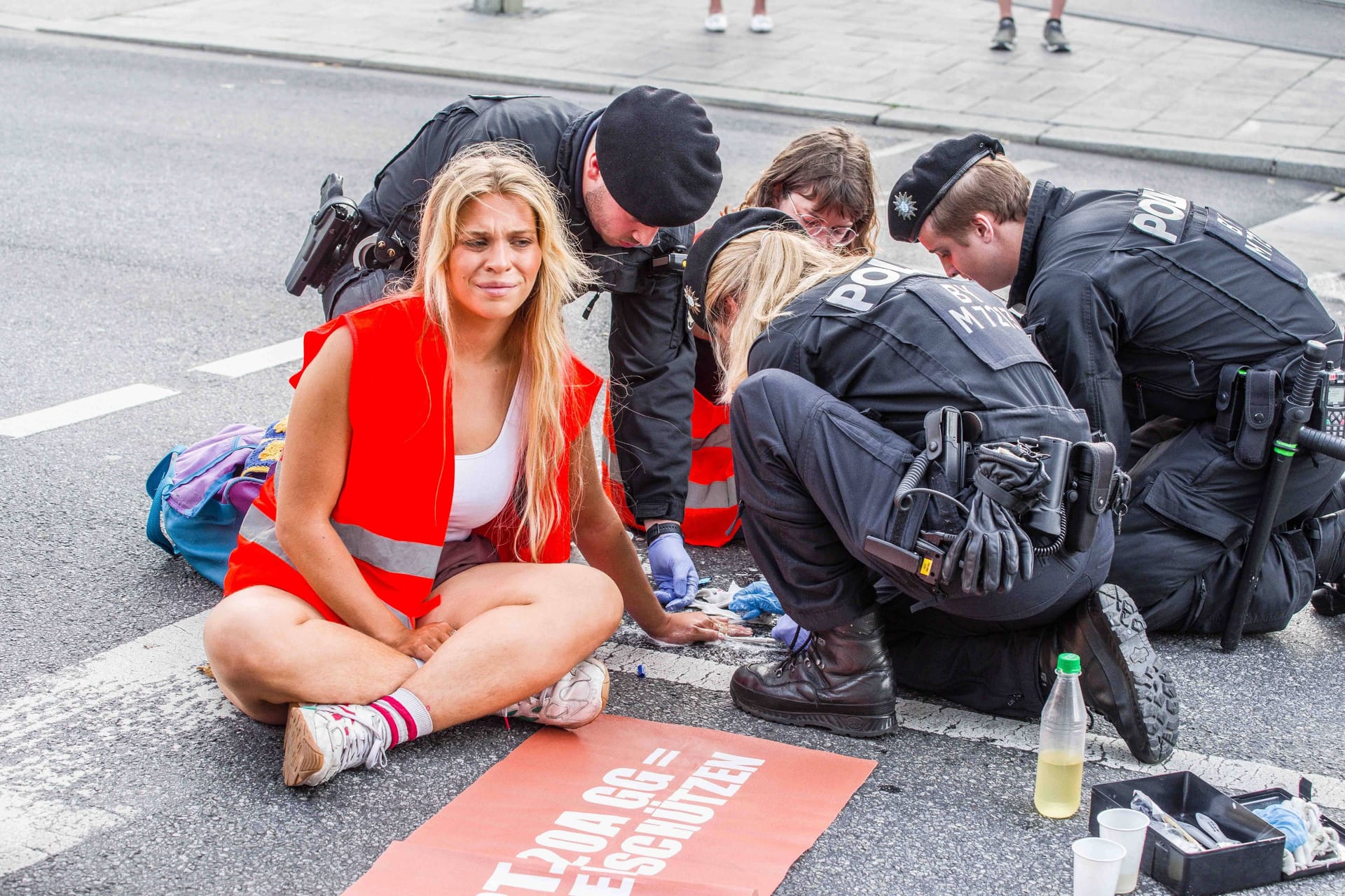 Ein Polizist versucht die Hand von Anja Windl von der Straße zu lösen: Die Klimaaktivisten will vor Gericht auf einen Anwalt verzichten.