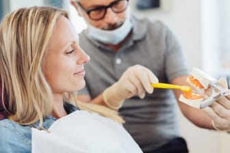 Zahnarzt zeigt Patientin die richtige Zahnputztechnik: Ob man Karies "wegputzen" kann, kommt auf das Stadium der Schmelzschädigung an.