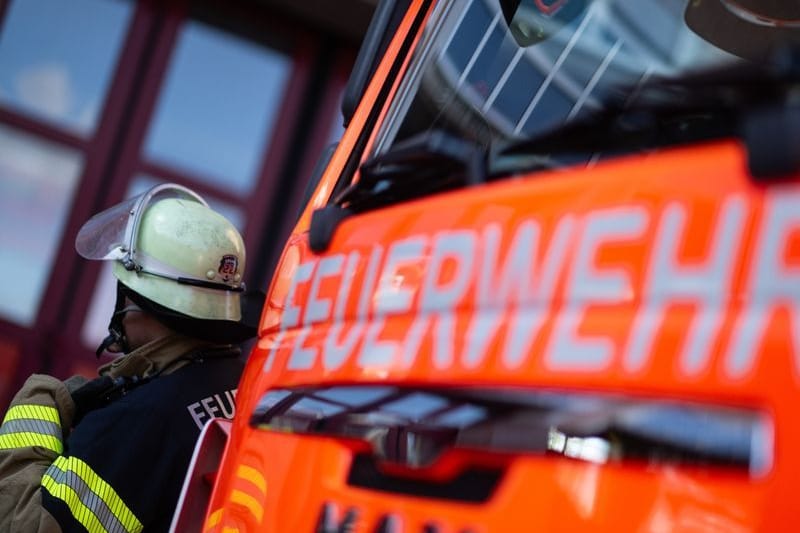 Eine Einsatzkraft der Feuerwehr steht neben einem Einsatzfahrzeug der Feuerwehr.