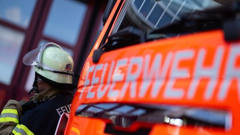 Eine Einsatzkraft der Feuerwehr steht neben einem Einsatzfahrzeug der Feuerwehr.