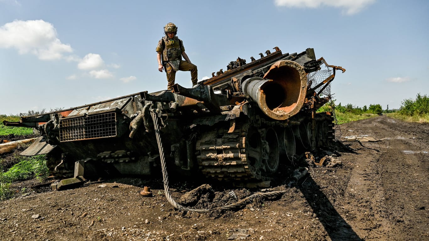 Ein ukrainischer Soldat steht auf einem zerstörten russischen Panzer. Moskau soll vor allem neuere Modelle in großem Ausmaß verlieren, so ein Bericht.