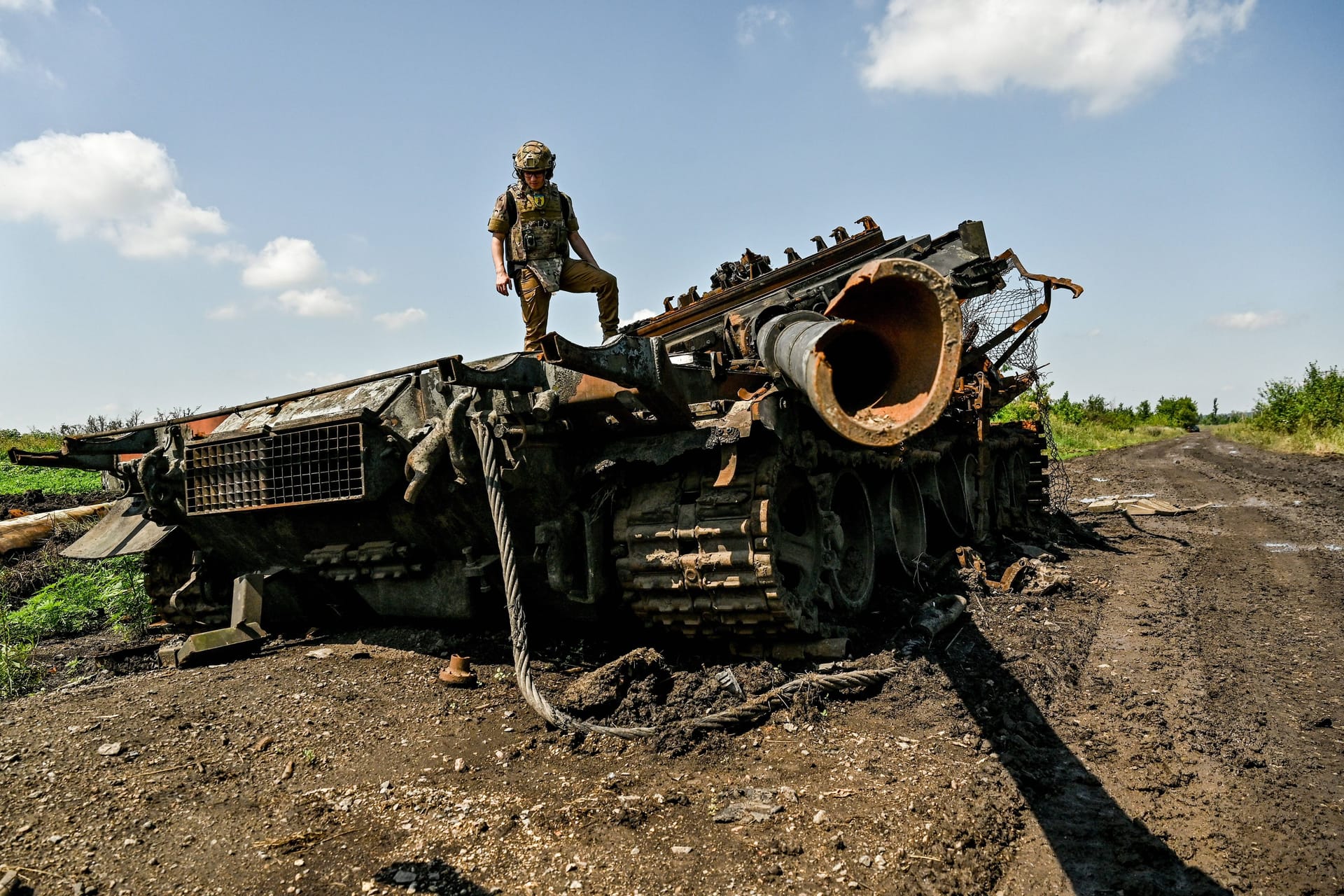 Ein ukrainischer Soldat steht auf einem zerstörten russischen Panzer. Moskau soll vor allem neuere Modelle in großem Ausmaß verlieren, so ein Bericht.