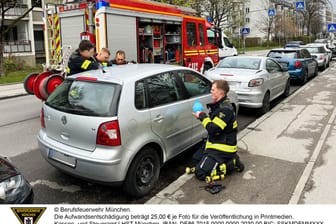 Drei Feuerwehrleute versuchen den Wagen zu öffnen, ein anderer lenkt den Jungen ab.