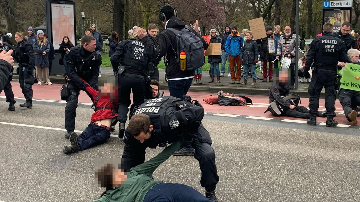 Klimaaktivisten werden am Kölner Ebertplatz von Einsatzkräften der Polizei von der Straße getragen.