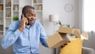 Dissatisfied disappointed buyer sitting at home on sofa in living room, man talking to online store support, holding cardboard box with parcel, wrong delivery damaged