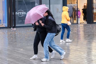 Zwei Frauen stemmen sich mit einem Regenschirm gegen den Wind (Symbolbild): In Düsseldorf warnt der Wetterdienst am Sonntag vor Sturmböen.