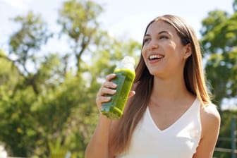 Healthy woman drinking green smoothie detox juice with kiwi mint kale outdoors