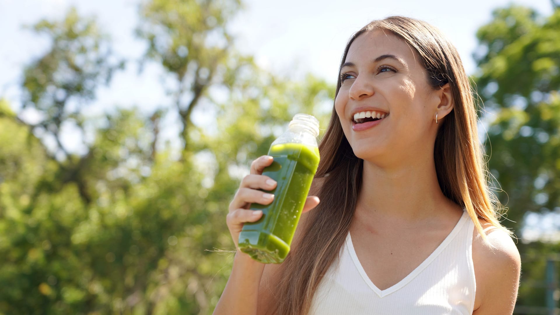 Healthy woman drinking green smoothie detox juice with kiwi mint kale outdoors