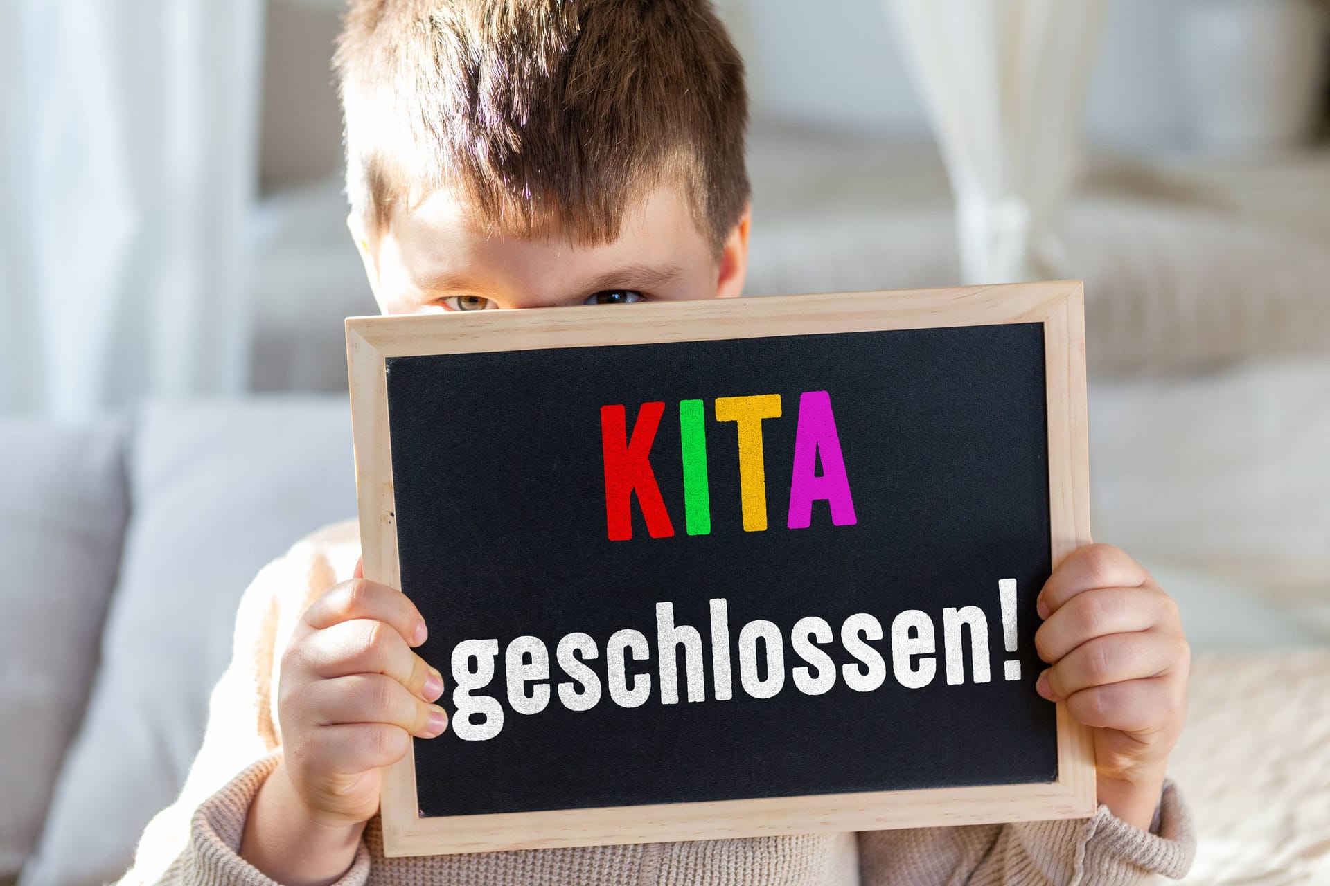 Ein Junge hält ein Schild mit "Kita geschlossen" (Montage): In der Region Hannover macht sich zunehmend Unmut bei Eltern breit.