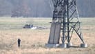 Ein verbrannter Strommast steht auf einem Feld und ein Polizeifotograf dokumentiert die Spuren. In der Tesla-Autofabrik in Grünheide steht die Produktion wegen des dadurch verursachten Stromausfalls still.