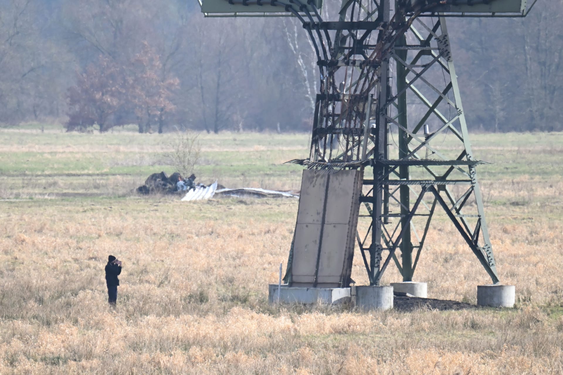 Ein verbrannter Strommast steht auf einem Feld und ein Polizeifotograf dokumentiert die Spuren. In der Tesla-Autofabrik in Grünheide steht die Produktion wegen des dadurch verursachten Stromausfalls still.