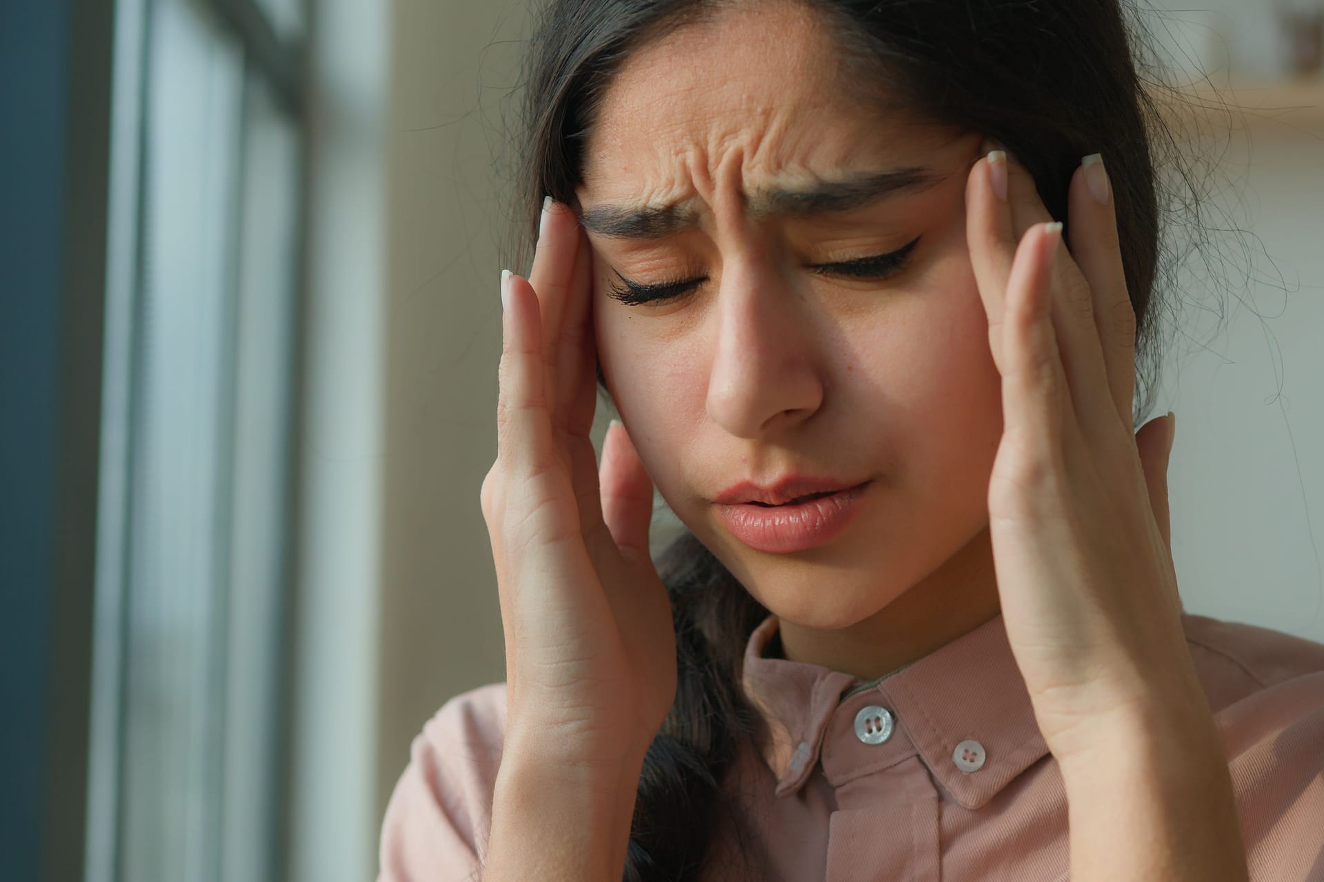 Tired sick woman arabian indian girl near window at home suffer from headache touch painful head migraine pain unhealthy ill female think difficult thoughts grief health disorder stress fatigue covid