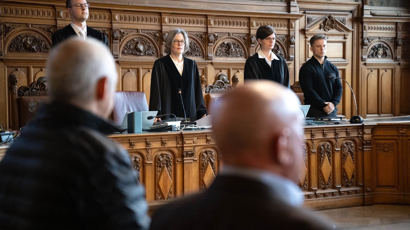 Der Angeklagte (l) steht vor Prozessbeginn im Gerichtssaal: Im Hintergrund ist die vorsitzende Richterin Gesa Kasper (3.v.l.) zu sehen – sie führt das Verfahren wegen Mordes.