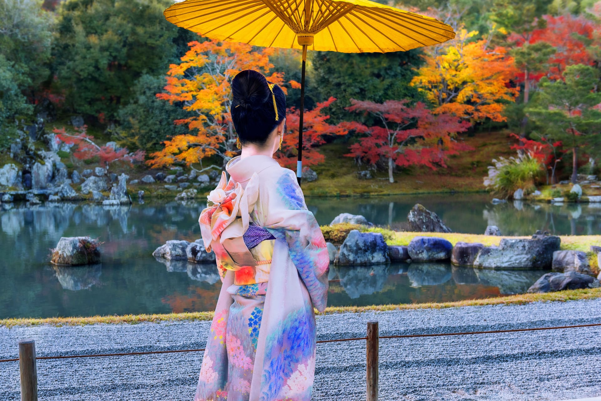 Woman in kimono with yellow umbrella in park during autumn.