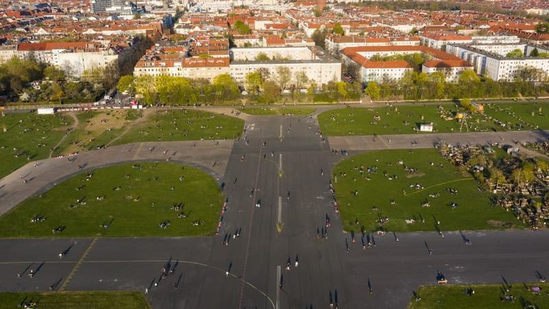 Zahlreiche Menschen sind während des Sonnenuntergangs auf dem Tempelhofer Feld unterwegs - im Hintergrund ist der Bezirk Neukölln zu sehen.