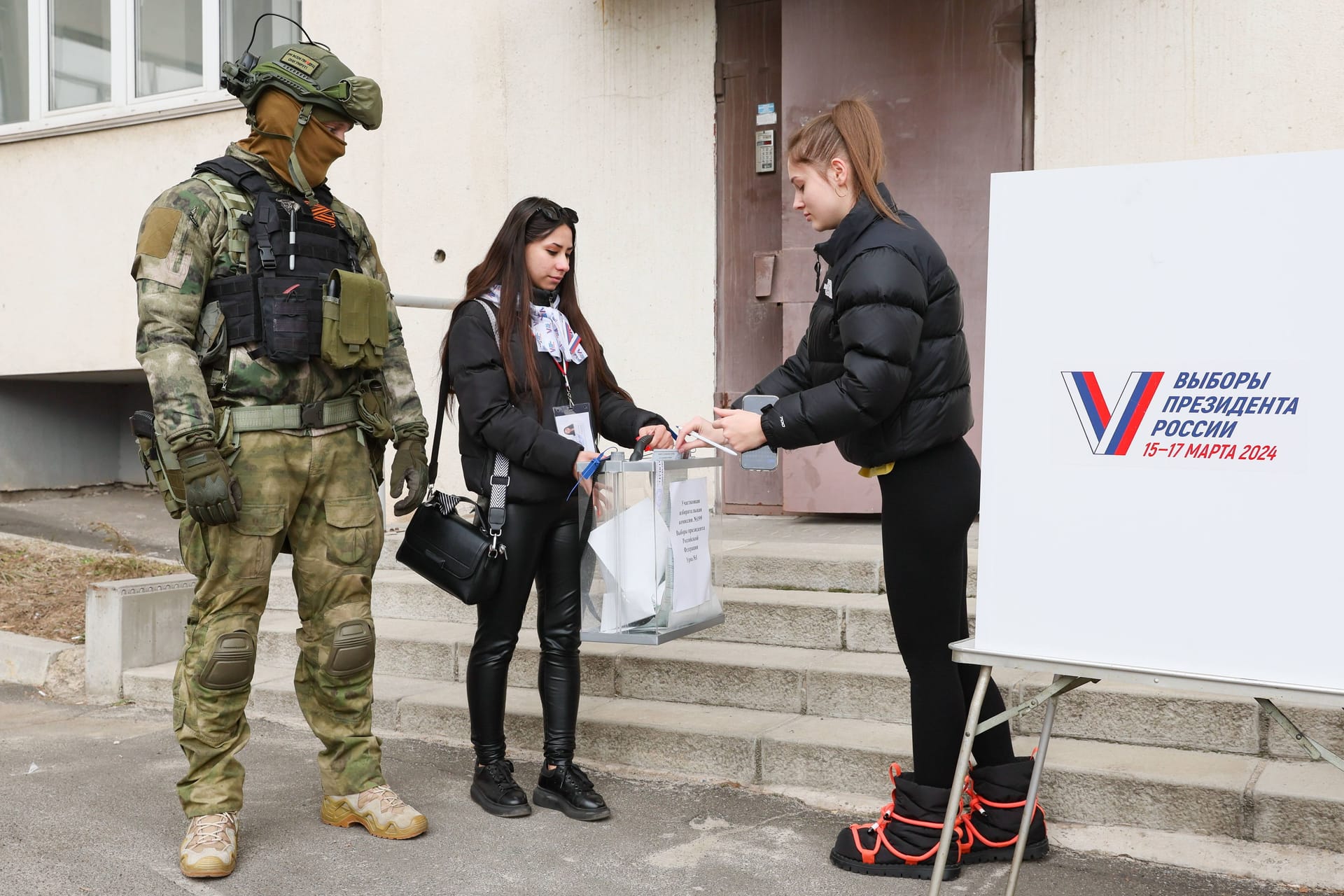 Eine Frau gibt in Donetsk ihren Stimmzettel ab, neben ihr ein russischer Soldat: Das russische Militär sucht die Menschen zu Hause auf, damit diese ihr Kreuz setzen.