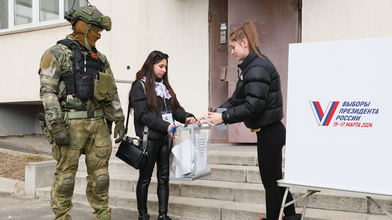 Eine Frau gibt in Donetsk ihren Stimmzettel ab, neben ihr ein russischer Soldat: Das russische Militär sucht die Menschen zu Hause auf, damit diese ihr Kreuz setzen.