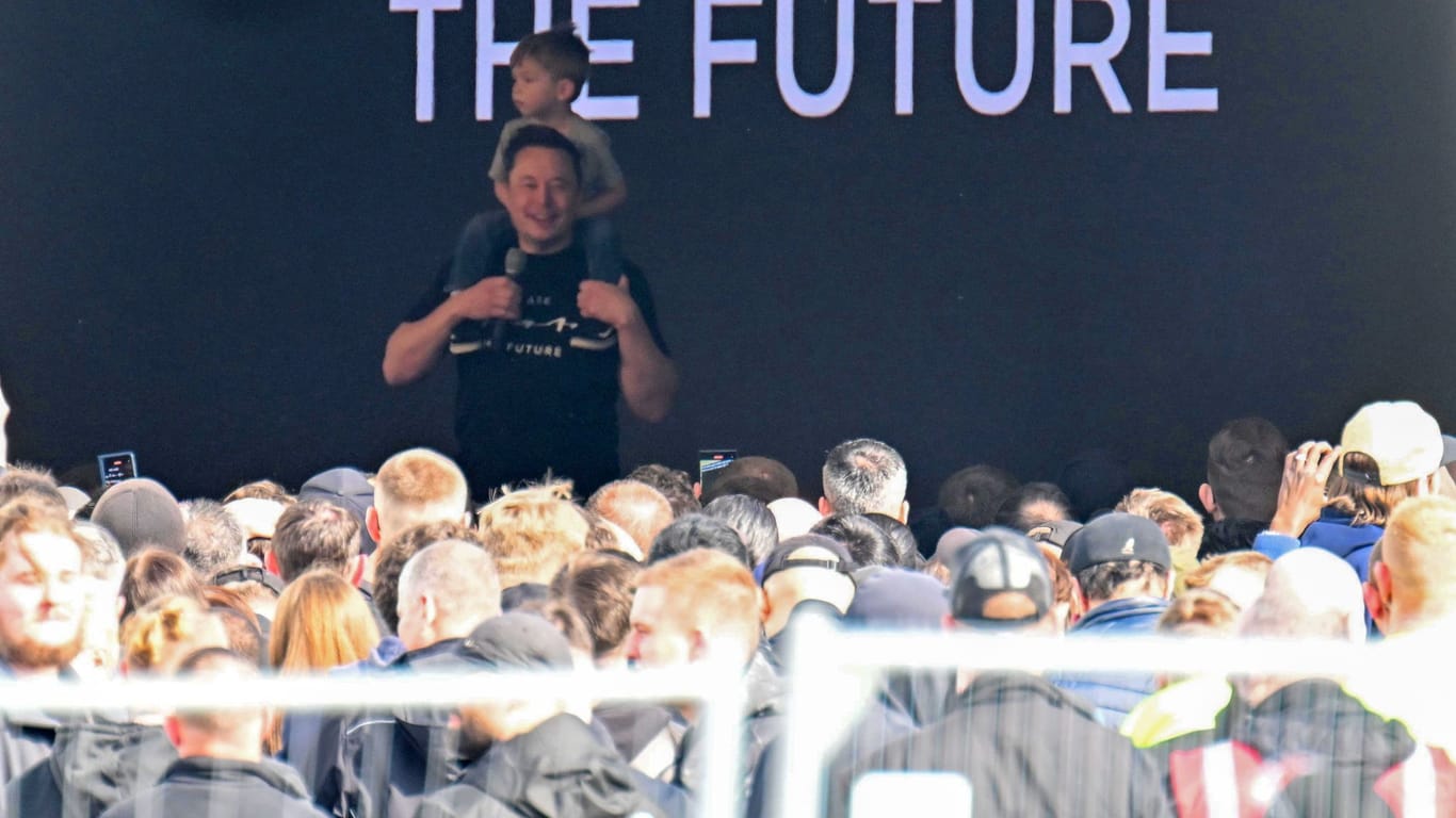 13.03.2024, Brandenburg, Grünheide: Tesla-Chef Elon Musk spricht in der Tesla Gigafactory Berlin-Brandenburg zu den Mitarbeitern und trägt dabei ein Kind auf den Schultern.