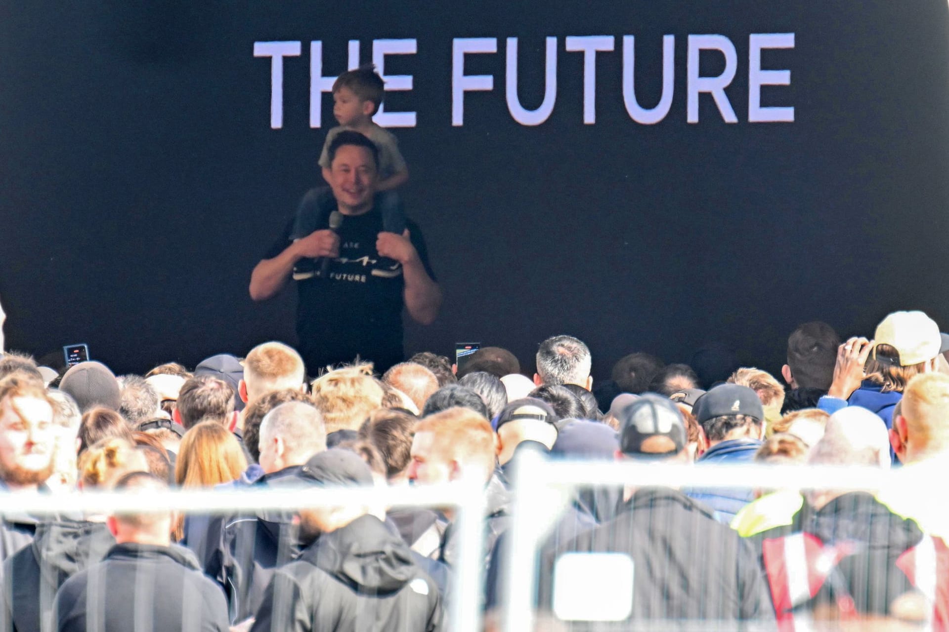 13.03.2024, Brandenburg, Grünheide: Tesla-Chef Elon Musk spricht in der Tesla Gigafactory Berlin-Brandenburg zu den Mitarbeitern und trägt dabei ein Kind auf den Schultern.