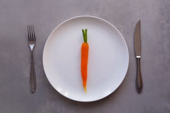 Eine einzelne Karotte liegt auf einem Teller: Fasten bedeutet, die Nahrungsaufnahme eine Zeit lang einzuschränken. Mit Vorerkrankungen kann das mitunter gefährlich werden.