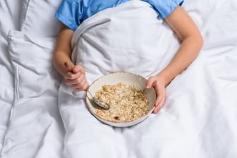 Person im Bett mit einem Teller Haferbrei