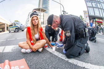 Ein Polizist versucht die Hand von Anja Windl von der Straße zu lösen: Die Klimaaktivisten will vor Gericht auf einen Anwalt verzichten.