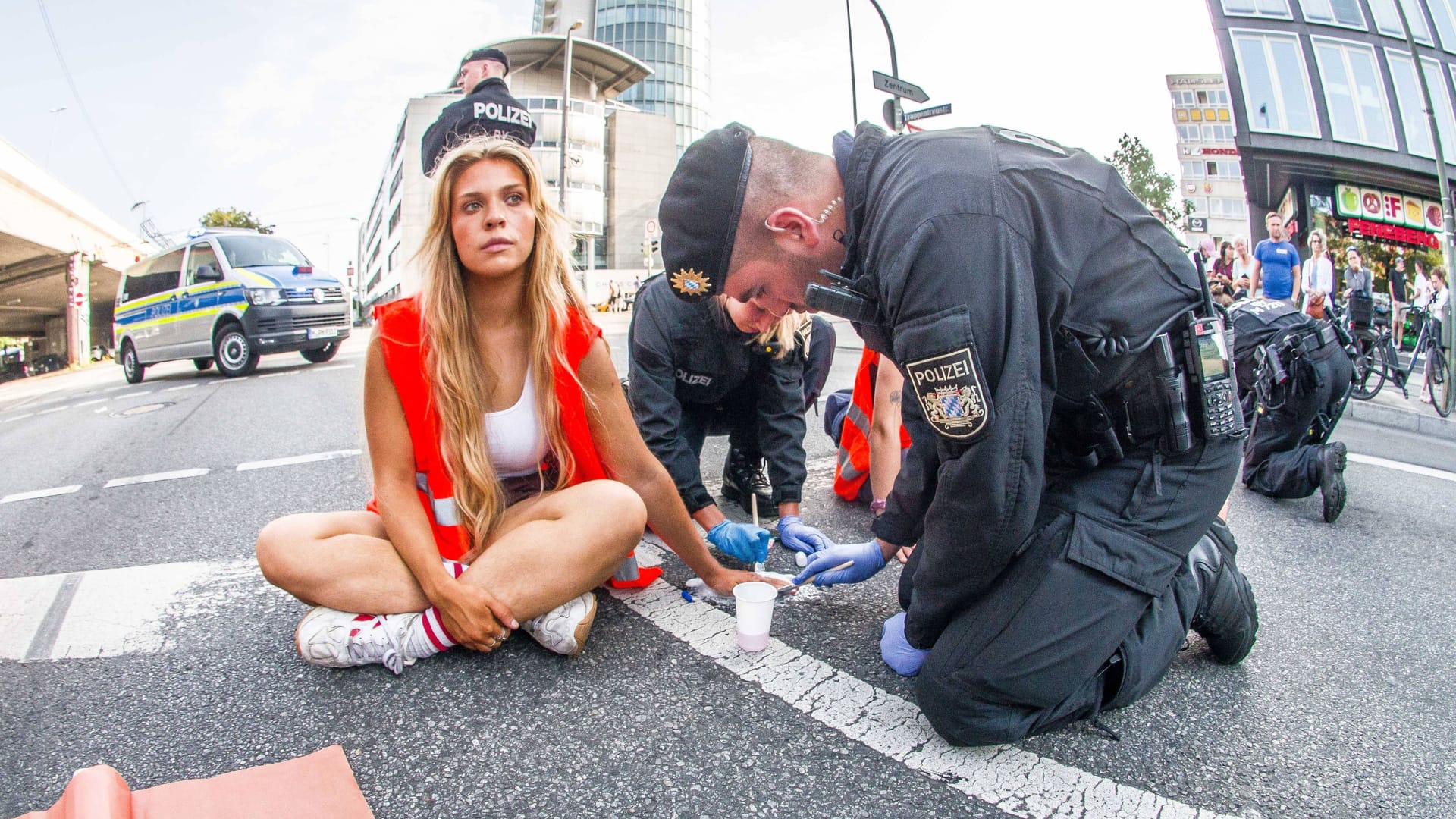 Ein Polizist versucht die Hand von Anja Windl von der Straße zu lösen: Die Klimaaktivisten will vor Gericht auf einen Anwalt verzichten.